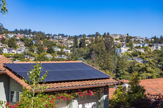 Zonnepanelen op het pannendak van een woonhuis, met groen en een blauwe lucht